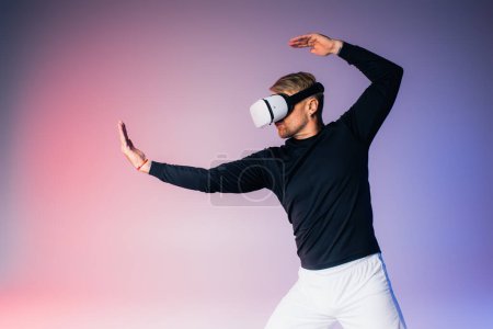 Téléchargez les photos : Un homme en chemise noire et pantalon blanc immergé dans la métaverse avec un casque VR dans un décor studio. - en image libre de droit