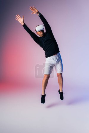 A man wearing a VR headset is jumping in the air while holding a virtual tennis racket in a studio setting.