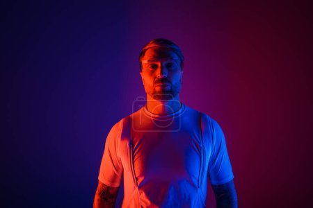Photo for A man in smart glasses stands confidently in front of a vibrant purple and blue background in a futuristic studio setting. - Royalty Free Image