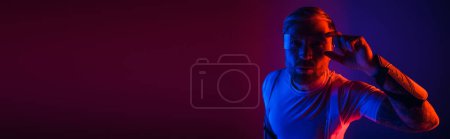 Téléchargez les photos : Un homme aux lunettes intelligentes se tient en confiance devant un fond rouge et bleu vibrant dans un décor de studio. - en image libre de droit