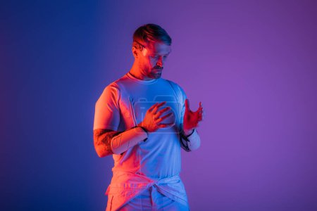 Un homme en lunettes intelligentes se tient en confiance dans un décor de studio sur un fond violet et bleu vibrant, évoquant un sentiment de réalité virtuelle.