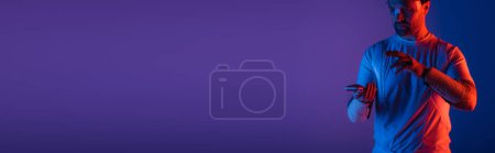 Photo for A man wearing smart glasses stands confidently in front of a vivid purple background, embodying a futuristic and virtual reality aesthetic. - Royalty Free Image
