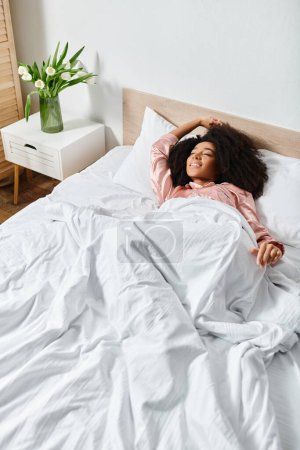 Mujer afroamericana rizada en pijama acostada en una cama con sábanas blancas, disfrutando de una mañana tranquila.