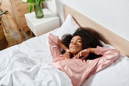 Una mujer afroamericana rizada en pijama, descansando pacíficamente sobre una cama blanca en un dormitorio soleado durante la mañana.