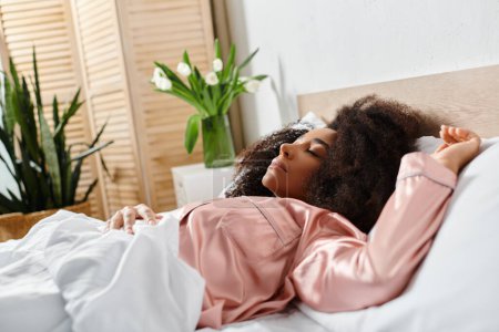 Eine lockige Afroamerikanerin im Schlafanzug entspannt sich morgens auf einem Bett neben einer üppigen grünen Pflanze in einem gemütlichen Schlafzimmer.
