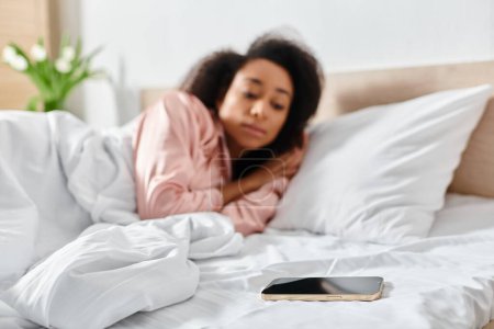 Una mujer afroamericana en pijama yace en la cama, absorbida en su teléfono celular a la suave luz de la mañana.