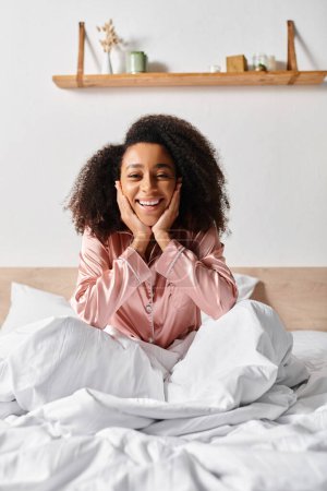Curly African American woman in pajamas relaxing on a white sheet-covered bed in the morning.