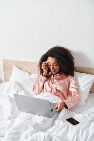 Femme afro-américaine bouclée en pyjama assise sur le lit, engagée dans une conversation téléphonique.