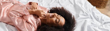 Téléchargez les photos : Femme afro-américaine bouclée en pyjama allongée sur le lit dans une scène du matin confortable. - en image libre de droit