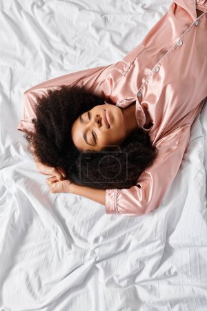 A curly African American woman in pajamas peacefully lays on a white bed in a bedroom. It is morning time.