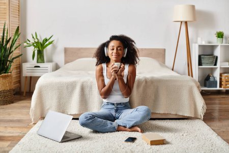 Una mujer afroamericana rizada en una camiseta sin mangas se sienta serenamente en el suelo frente a una cama moderna.