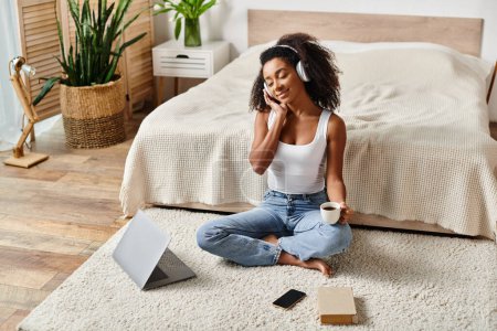 Téléchargez les photos : Curly African American woman in a tank top sitting on the floor, engaged in a phone conversation in a modern bedroom. - en image libre de droit