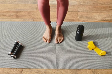Photo for African American woman in active wear standing on a yoga mat with a pair of feet beside her. - Royalty Free Image