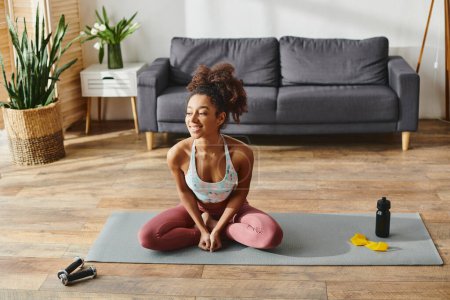 Lockige Afroamerikanerin in aktiver Kleidung praktiziert Yoga in gemütlicher Wohnzimmeratmosphäre.