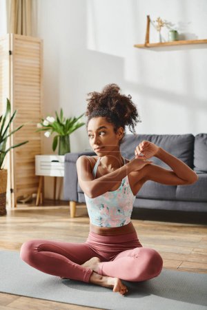 A curly African American woman in activewear practices yoga in her living room, embodying balance and strength.