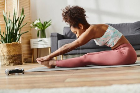 Une afro-américaine frisée en tenue de sport pratique le yoga sur le sol, respirant calme et concentration.