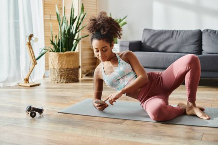 A curly African American woman in activewear gracefully striking a yoga pose on a yoga mat at home.