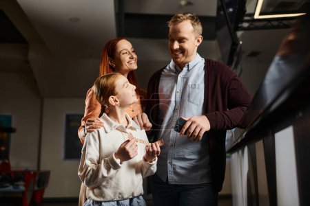 A man and a woman stand together with daughter, embodying unity and love, enjoying a special moment at the cinema as a happy family.