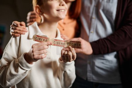 Téléchargez les photos : Enfant tenir joyeusement une bande colorée, symbolisant l'unité et le lien avec la famille lors d'une sortie au cinéma. - en image libre de droit