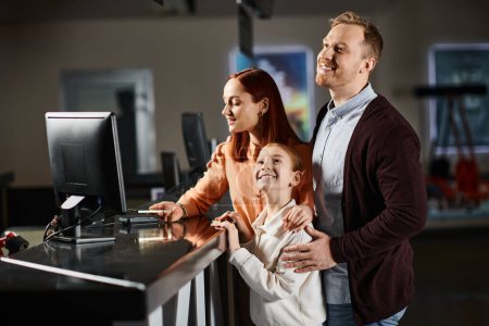 Ein Paar, das mit seinem Kind vor einem Computer steht, vertieft in alles, was auf dem Bildschirm zu sehen ist, und sich an die Technologie bindet.