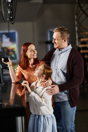 Mann, Frau und Kind stehen vor einem Computerbildschirm, vertieft in eine gemeinsame Aktivität.