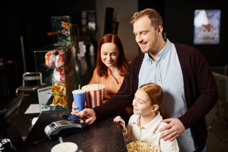 A father and his daughter happily enjoy popcorn at a table during a fun family movie night at the cinema.