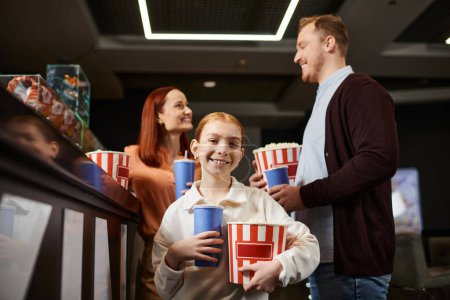 Famille heureuse debout ensemble, tenant des tasses, profitant d'une sortie cinéma.