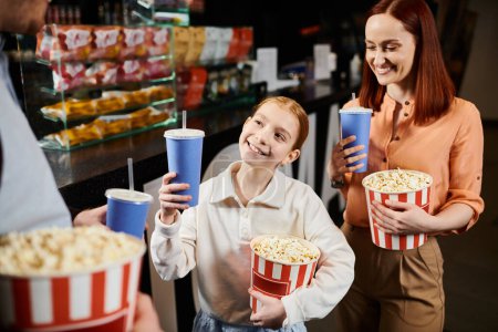 Una familia feliz de pie en un círculo, sosteniendo cubos de palomitas de maíz en el cine.