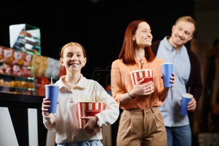 Une famille heureuse profitant d'un moment de collage au cinéma, debout ensemble et tenant des tasses.