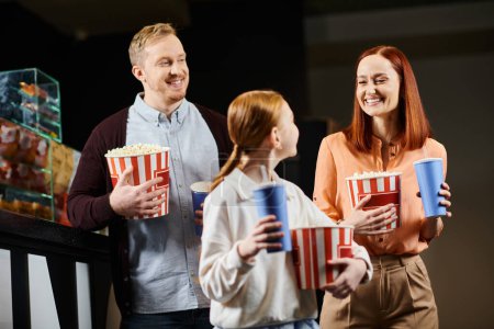 Una familia feliz de pie, cada uno sosteniendo un cubo de palomitas de maíz en el cine.