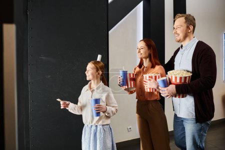 Téléchargez les photos : Une famille heureuse se tient à proximité, tenant du pop-corn dans un décor de cinéma, profitant d'un moment joyeux ensemble. - en image libre de droit