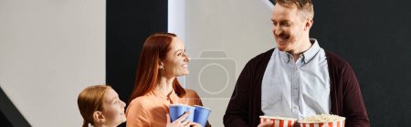 Photo for A happy family enjoying a movie night, holding popcorn in their hands. - Royalty Free Image