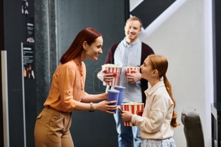Eine Frau reicht einem kleinen Mädchen während eines Familienausflugs im Kino freundlich einen Eimer Popcorn.