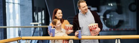 A man and his family happily eat popcorn while enjoying a movie night together at the cinema.