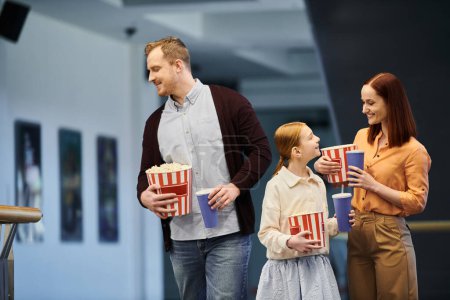 Foto de A happy family standing together, holding buckets of popcorn. - Imagen libre de derechos