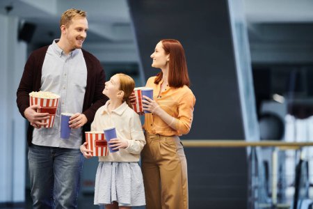 Eine glückliche Familie steht im Kreis, jede hält eine Schachtel Popcorn im Kino und genießt einen lustigen Kinoabend zusammen.