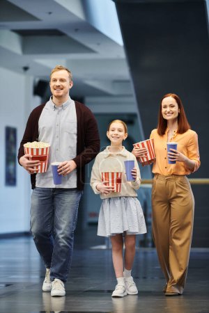 Un hombre, una mujer y un niño caminando felizmente por un pasillo en un cine, disfrutando de un tiempo familiar de calidad juntos.