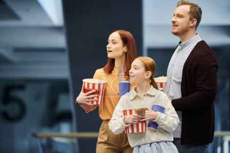 Téléchargez les photos : Un homme et sa famille tiennent joyeusement des tasses de pop-corn, profitant d'une sortie en famille au cinéma. - en image libre de droit