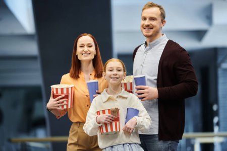 Un hombre, una mujer y un niño felices sosteniendo palomitas de maíz en un cine, disfrutando de un tiempo de calidad juntos.