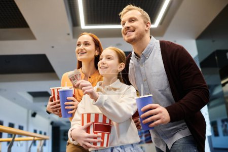 Téléchargez les photos : Une famille heureuse se tient ensemble tenant des tasses, profitant de leur temps au cinéma. - en image libre de droit