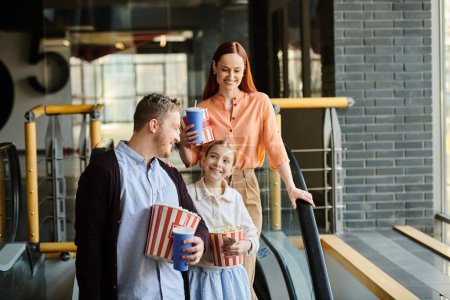 Téléchargez les photos : Un homme, une femme et un enfant se tiennent devant un cinéma, excités de passer du temps en famille ensemble pour regarder un film. - en image libre de droit