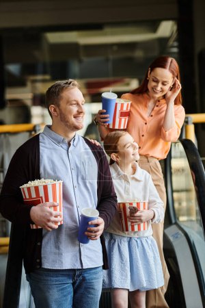 Photo for Family enjoy popcorn while walk down the escalator, at the cinema, bonding as a happy family. - Royalty Free Image