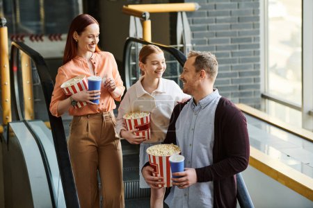 A happy family stands grouped together, each holding buckets of popcorn, enjoying a movie outing at the cinema.