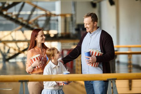 Un homme, une femme et un enfant joyeux tiennent du pop-corn au cinéma.