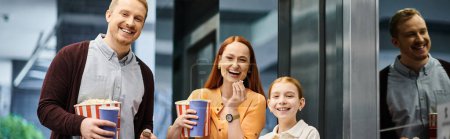 Téléchargez les photos : Une famille heureuse debout dans un cinéma, profitant d'un moment de convivialité avant de regarder un film. - en image libre de droit
