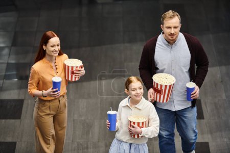 Eine Familie spaziert fröhlich eine Straße entlang und hält nach einem lustigen Kinobesuch Eimer mit Popcorn in der Hand