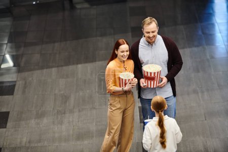 A happy family at the cinema, holding a bucket of popcorn and enjoying a movie together.