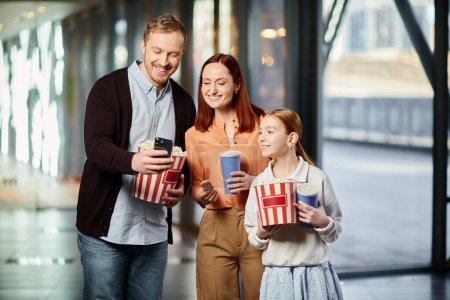 famille tenant joyeusement des boîtes de pop-corn au cinéma, collant ensemble