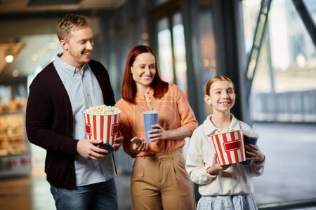 A man, woman, and child happily holding popcorn boxes, enjoying a family outing at the cinema.
