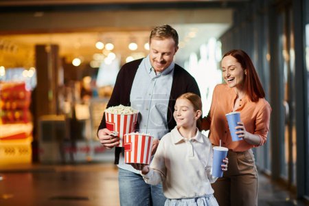 A man, woman and a child happily holding popcorn at the cinema, enjoying quality time together.